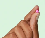 Hand holding one DulcoLax For Women tablet to show the colour and size, in front of a light green background