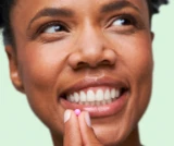 Close up shot of a smiling woman about to take one tablet of DulcoLax For Women in front of a light green background