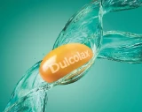 Dulcolax pill surrounded by splashing water on a turquoise background.