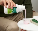 Person pouring pink Dulcolax Liquid Cherry into a measuring cup on a table.