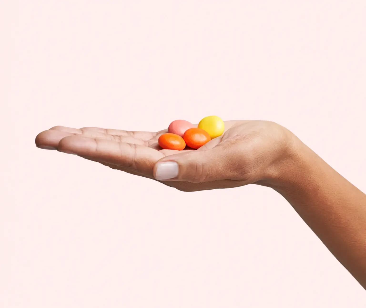 A hand holding colorful round candies against a plain background.