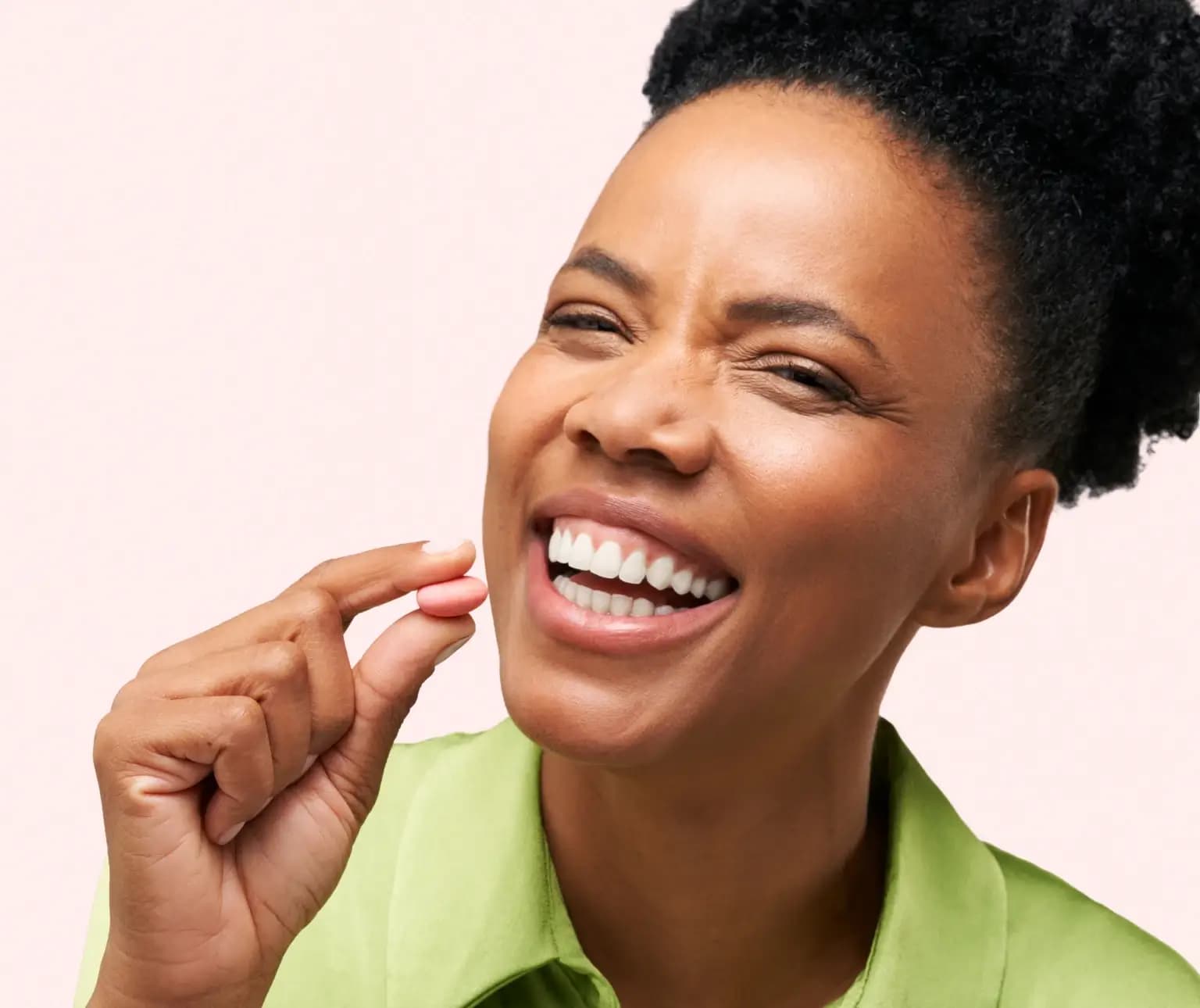 Person smiling and holding a pink pill between fingers.