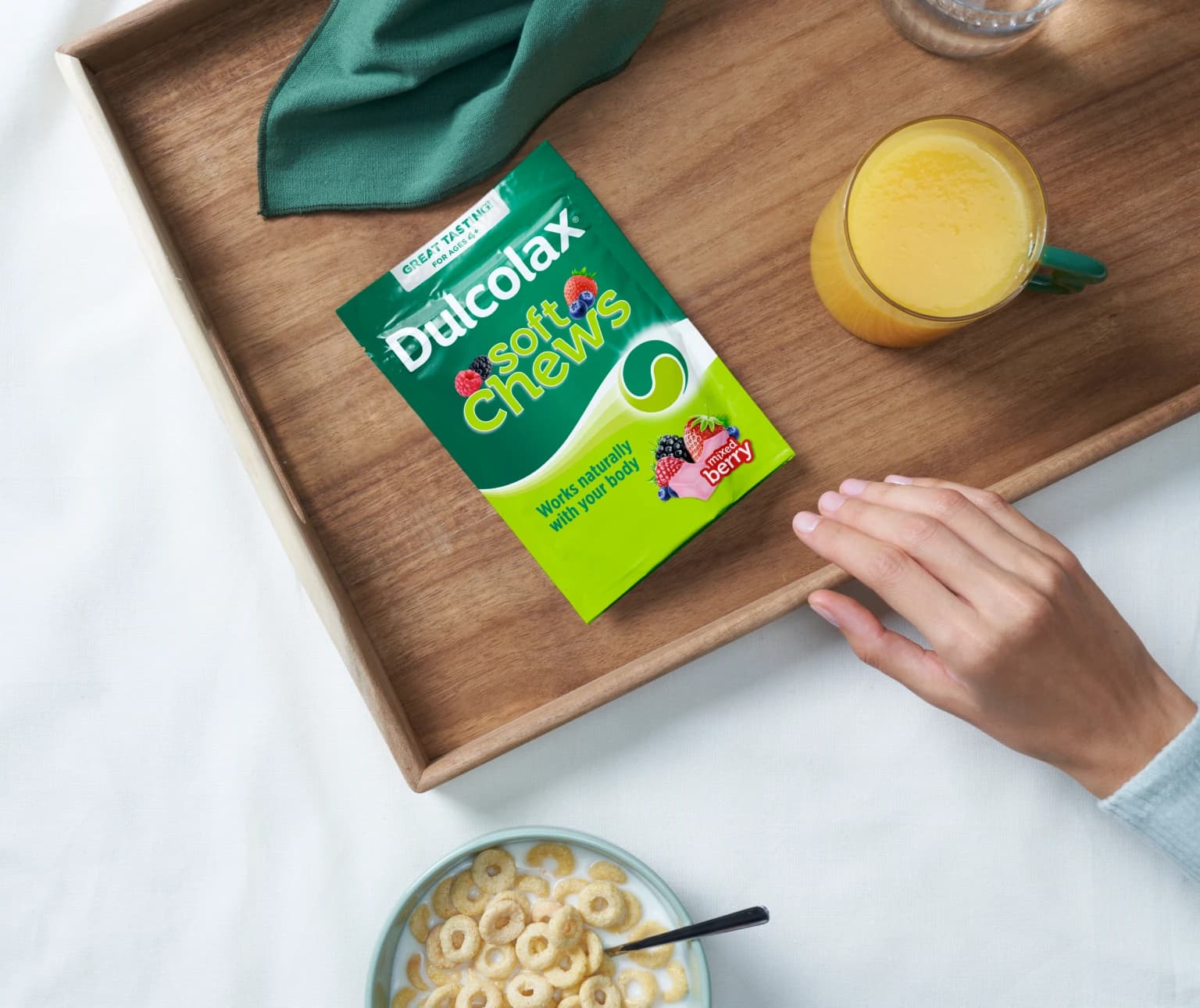 Dulcolax soft chews mixed berry on a tray with a hand, a bowl of cereal, and juice.