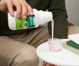 Person pouring pink Dulcolax Liquid Cherry into a measuring cup on a table.
