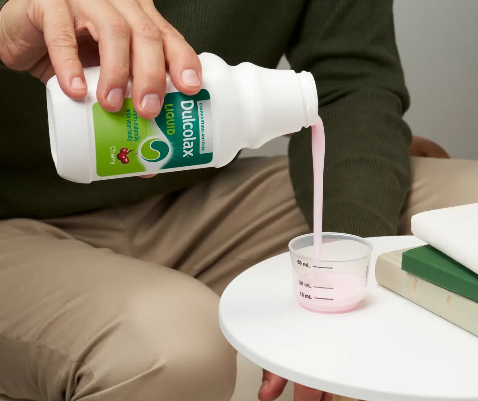 Person pouring pink Dulcolax Liquid Cherry into a measuring cup on a table.