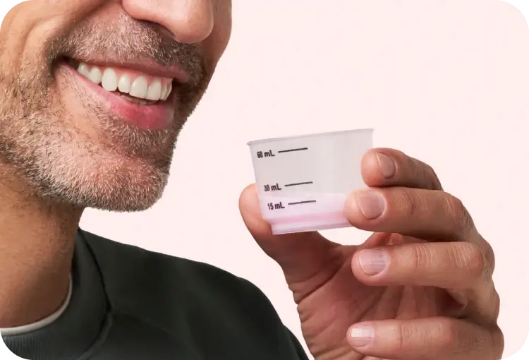 Person holding a 60 mL measuring cup with liquid, smiling slightly.