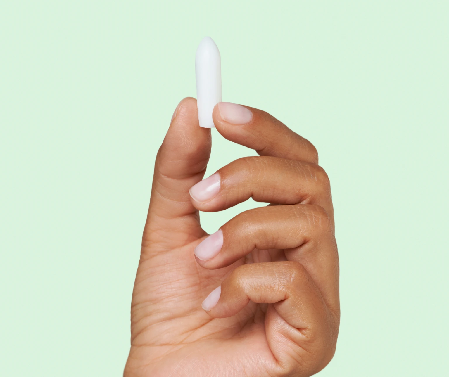 A hand holds a white suppository against a light green background.