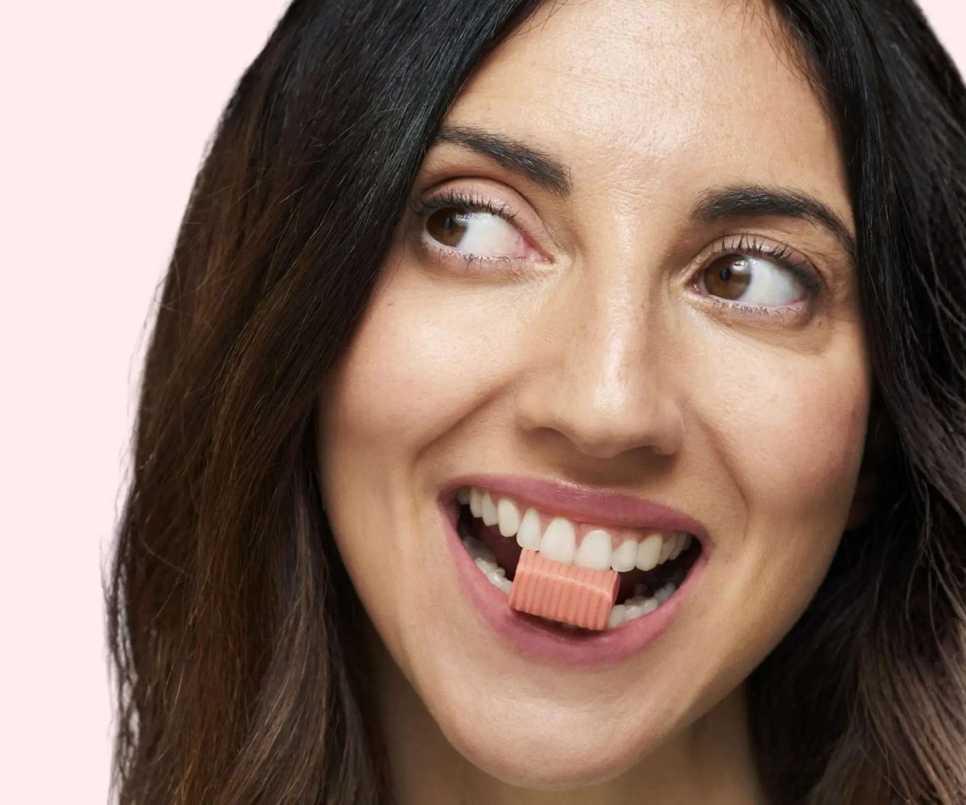 Woman smiling while holding a pill near her mouth.