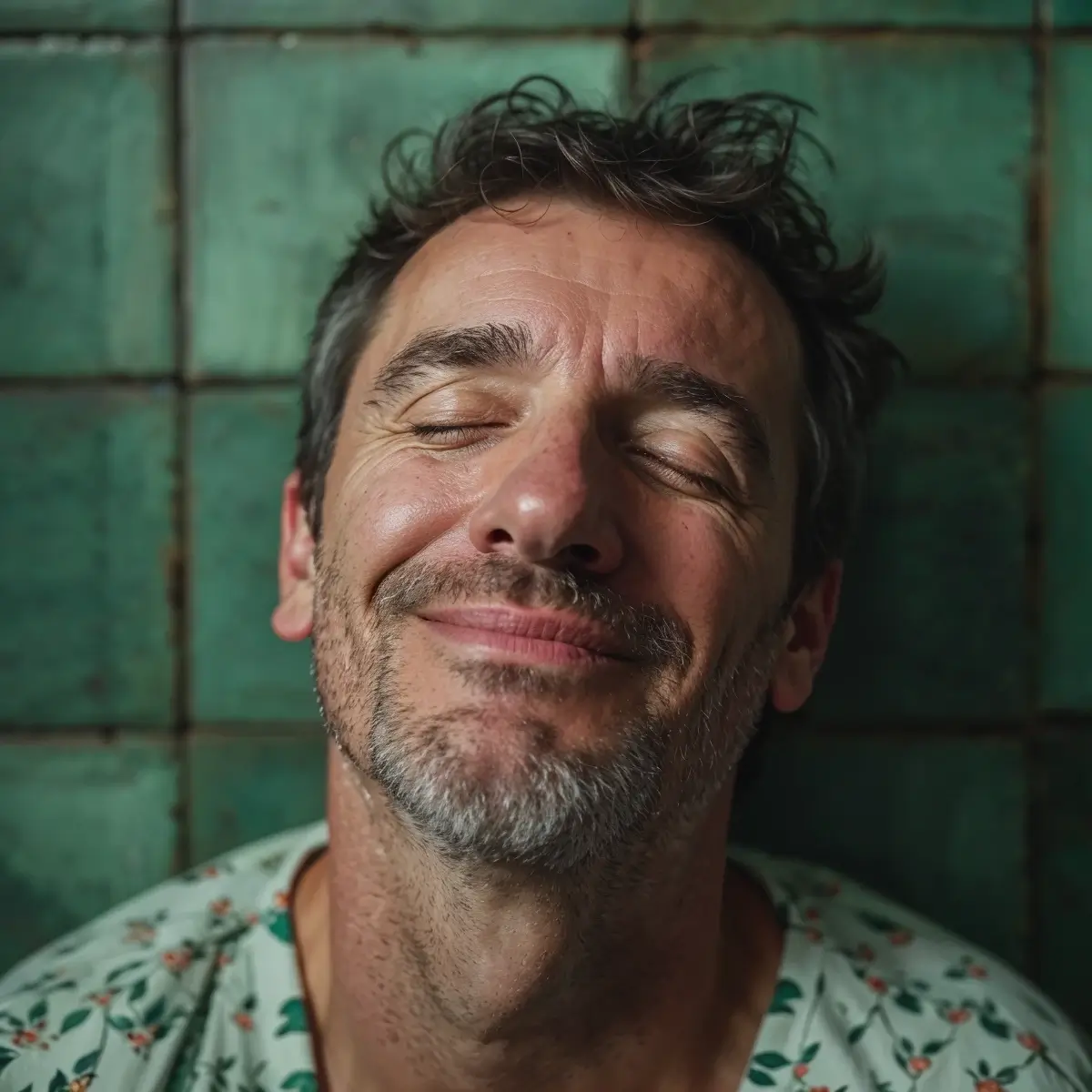 A man with closed eyes smiles contentedly against a green tiled background.