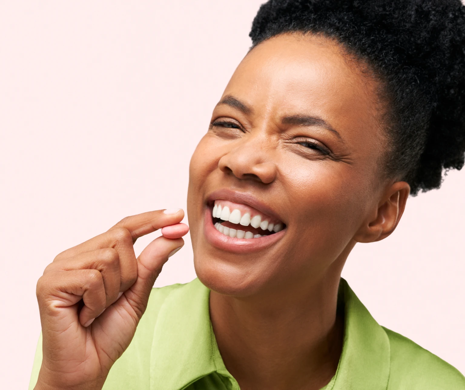 Person smiling and holding a pink pill between fingers.