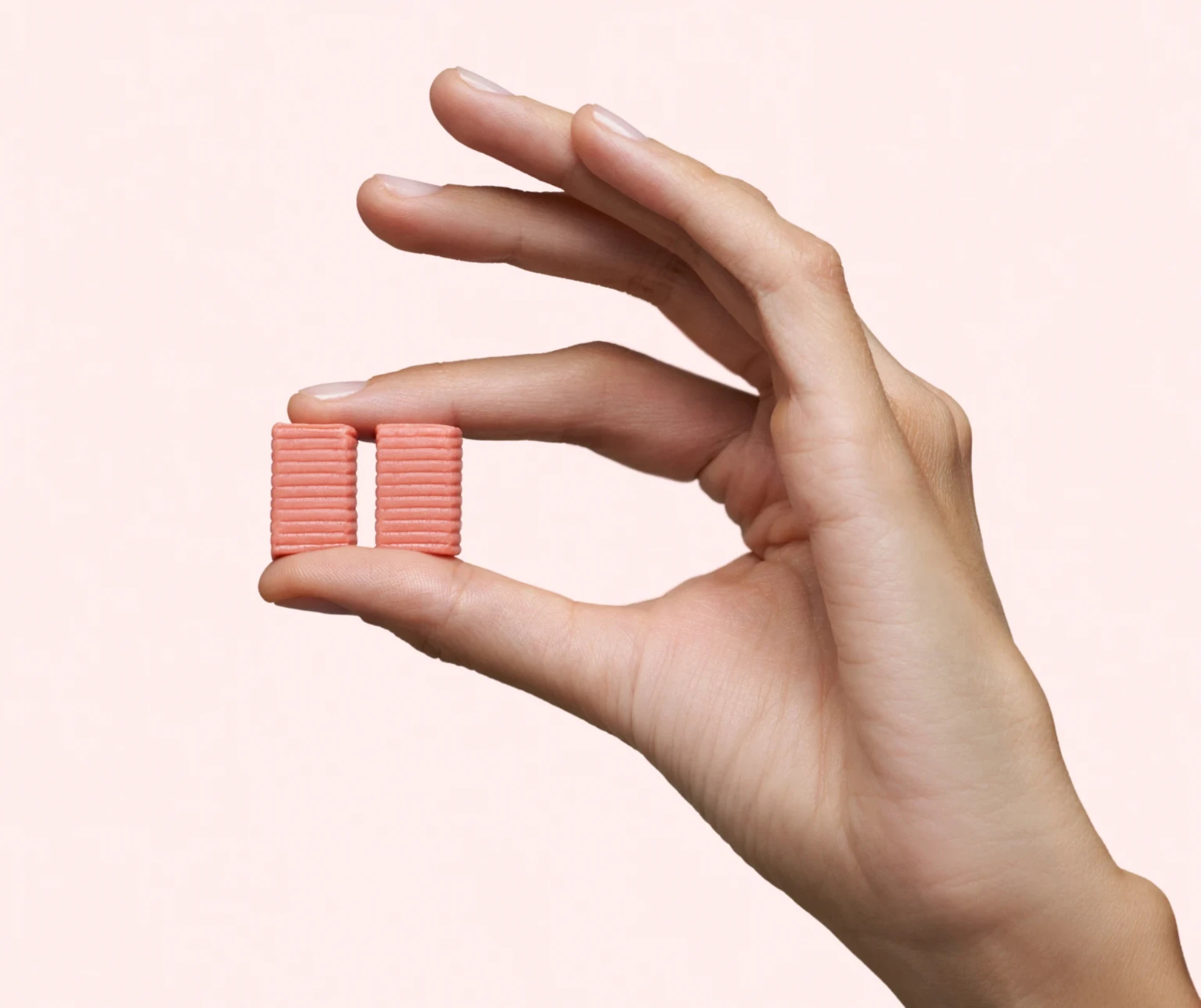 Main qui tient deux morceaux de DulcoLax Soft Chews pour montrer la couleur et la taille, devant un fond rose pâle