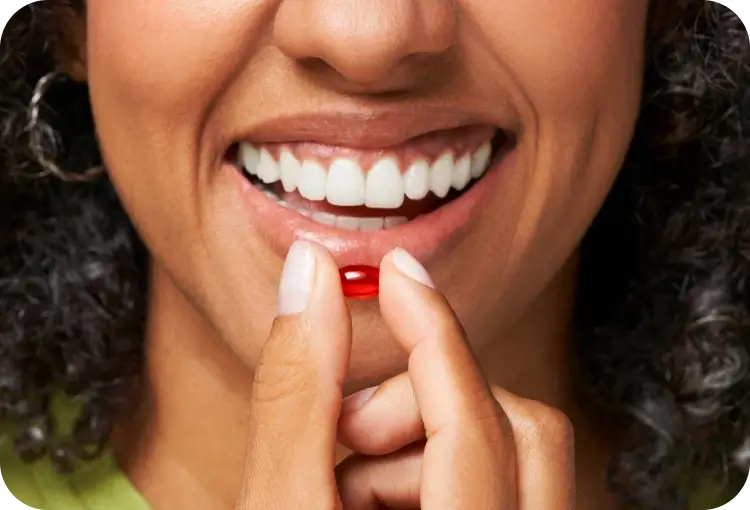 A person smiling while holding a red capsule close to their lips.