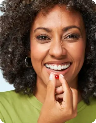 Person smiling, holding a small red capsule near their mouth.