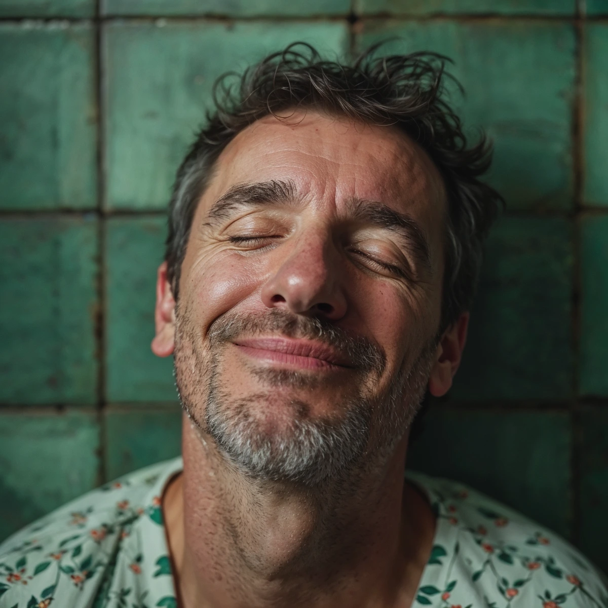 A man with closed eyes smiles contentedly against a green tiled background.