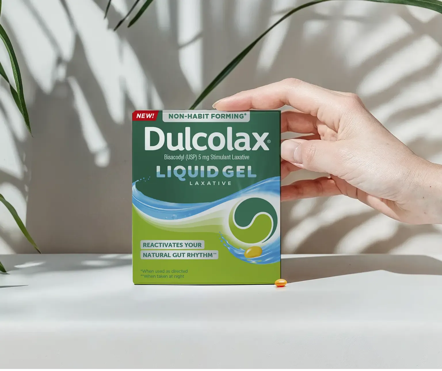 Dulcolax Liquid Gel Laxative, Bisacodyl 5mg, held in hand with sunlight and plant shadows.