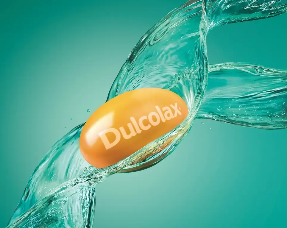 Dulcolax pill surrounded by splashing water on a turquoise background.