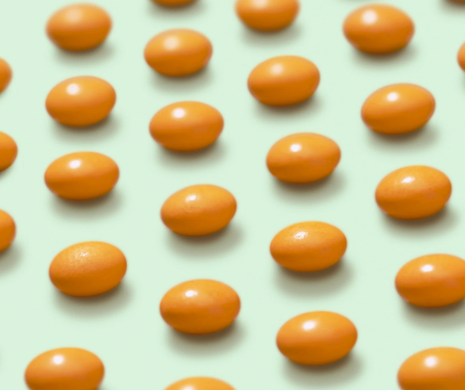 Orange pills arranged in neat rows on a light green background.