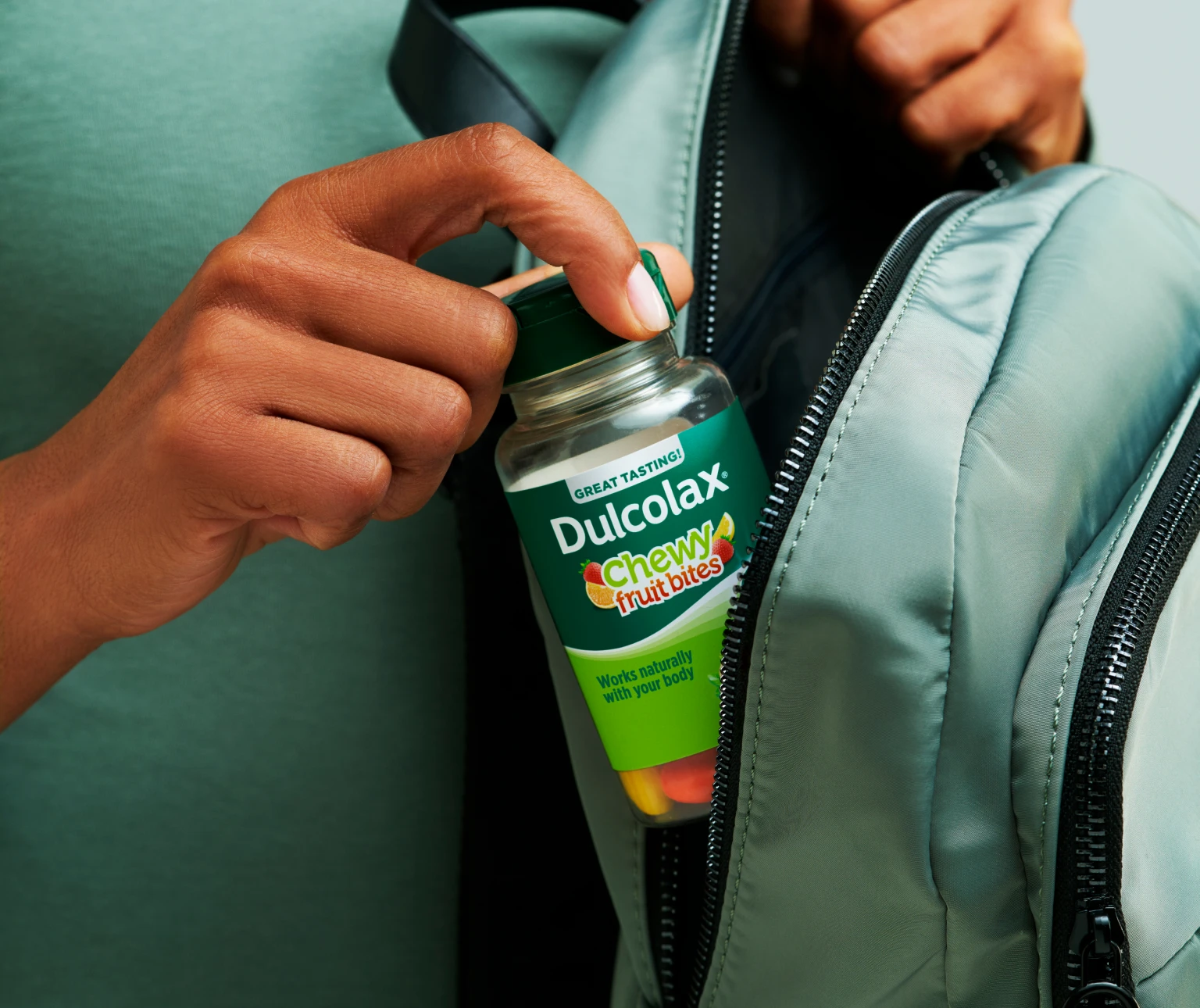 Hand placing Dulcolax Chewy Fruit Bites into a backpack pocket.