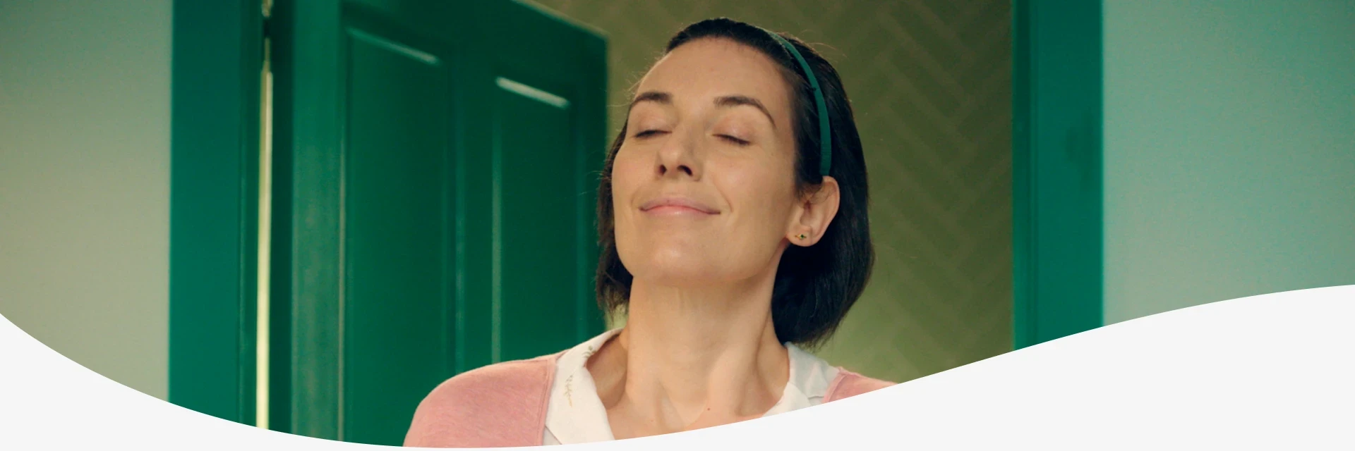 A woman in a pink cardigan appears relaxed with her eyes closed and a content expression.