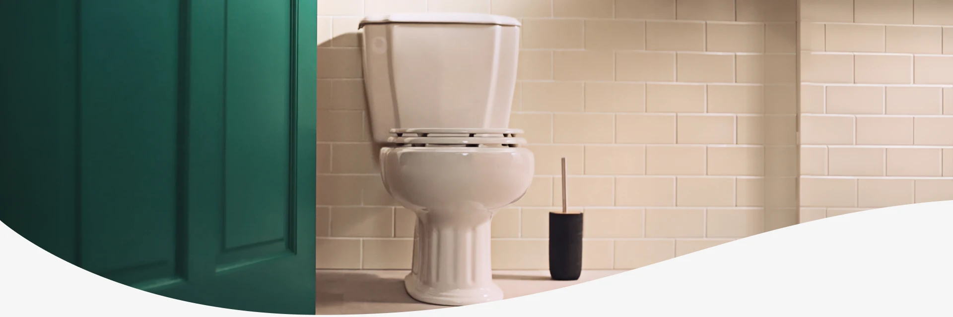 Toilet and brush set next to tiled bathroom wall.