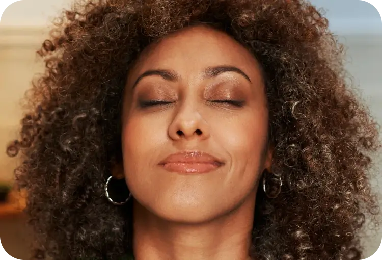 Woman with curly hair smiling with eyes closed, appearing relaxed.