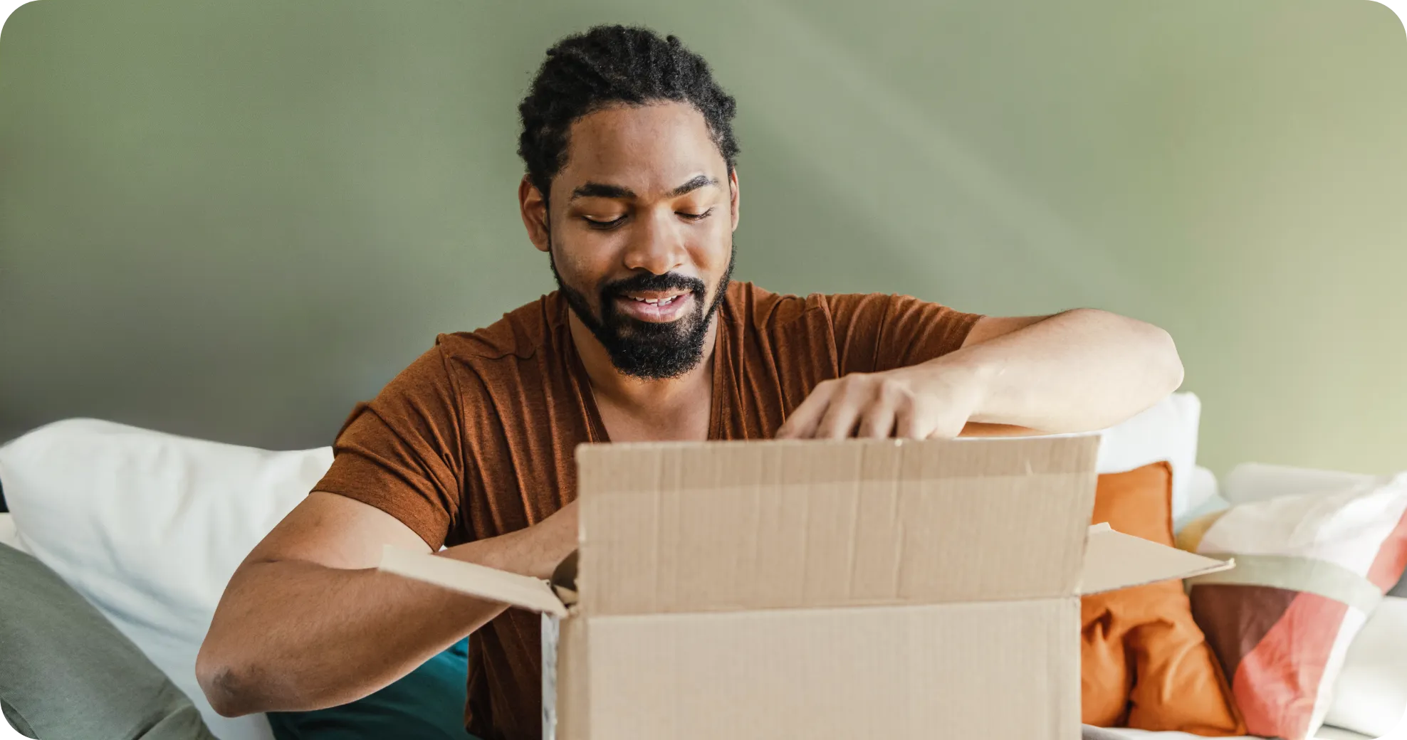 Person opening a cardboard box while sitting on a sofa with colorful cushions.