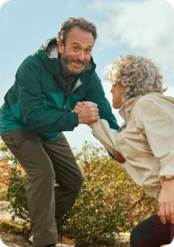 A man helps a woman up a hill while they are hiking outdoors.