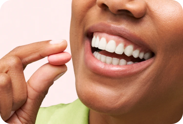 Person smiling while holding a pink pill near their mouth.
