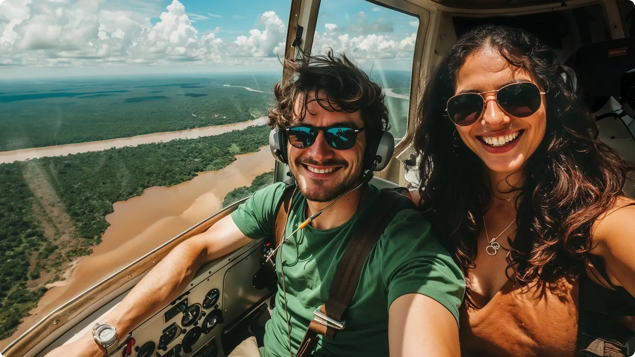 Two people smiling inside a helicopter with a scenic river view outside.
