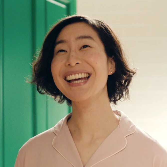 Smiling person in pink shirt against a green door background.