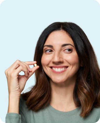 Woman holding a small yellow and white capsule, smiling with a relaxed expression.