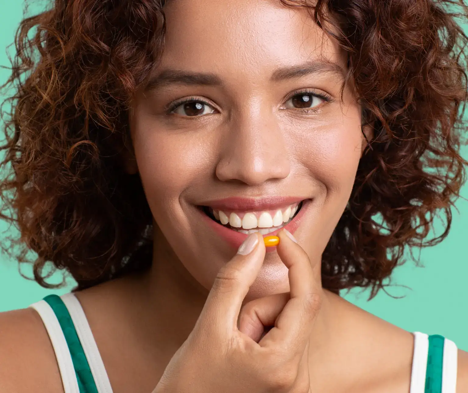 Smiling woman holding a small yellow-orange capsule near her mouth.