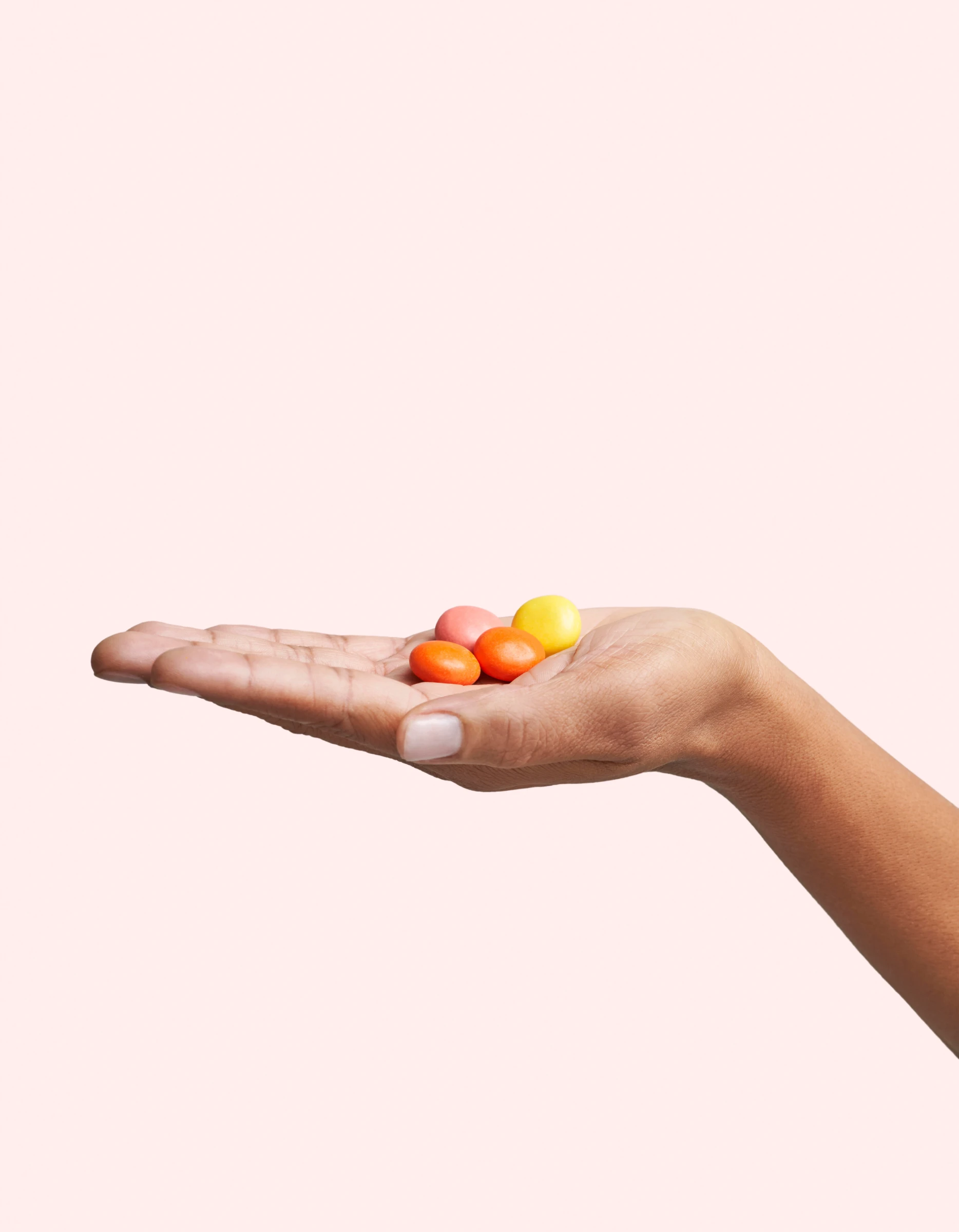 Hand holding colorful small round pills on a light background.