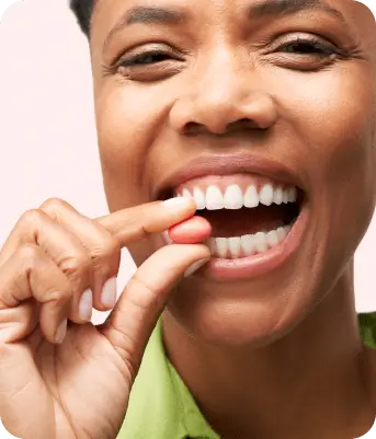 Person smiling while holding a pink pill near their mouth.