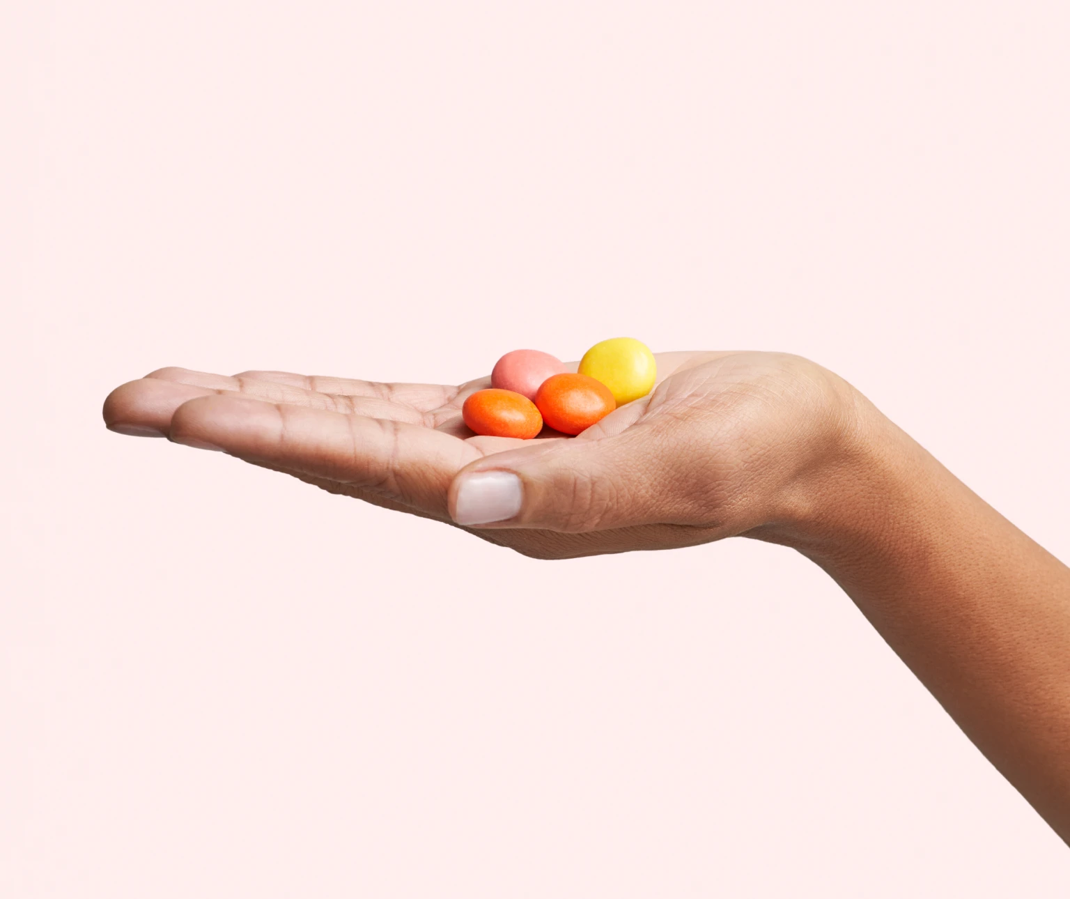 A hand holding colorful round candies against a plain background.