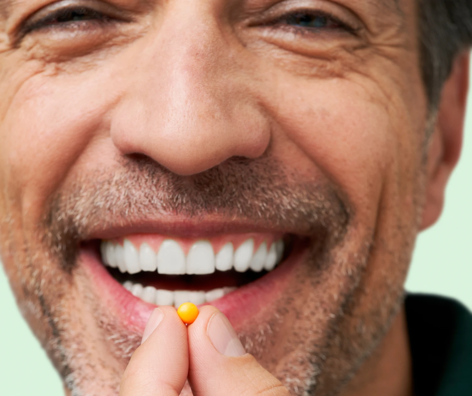 Close up shot of a smiling man about to take one tablet of DulcoLax Tablets in front of a light green background