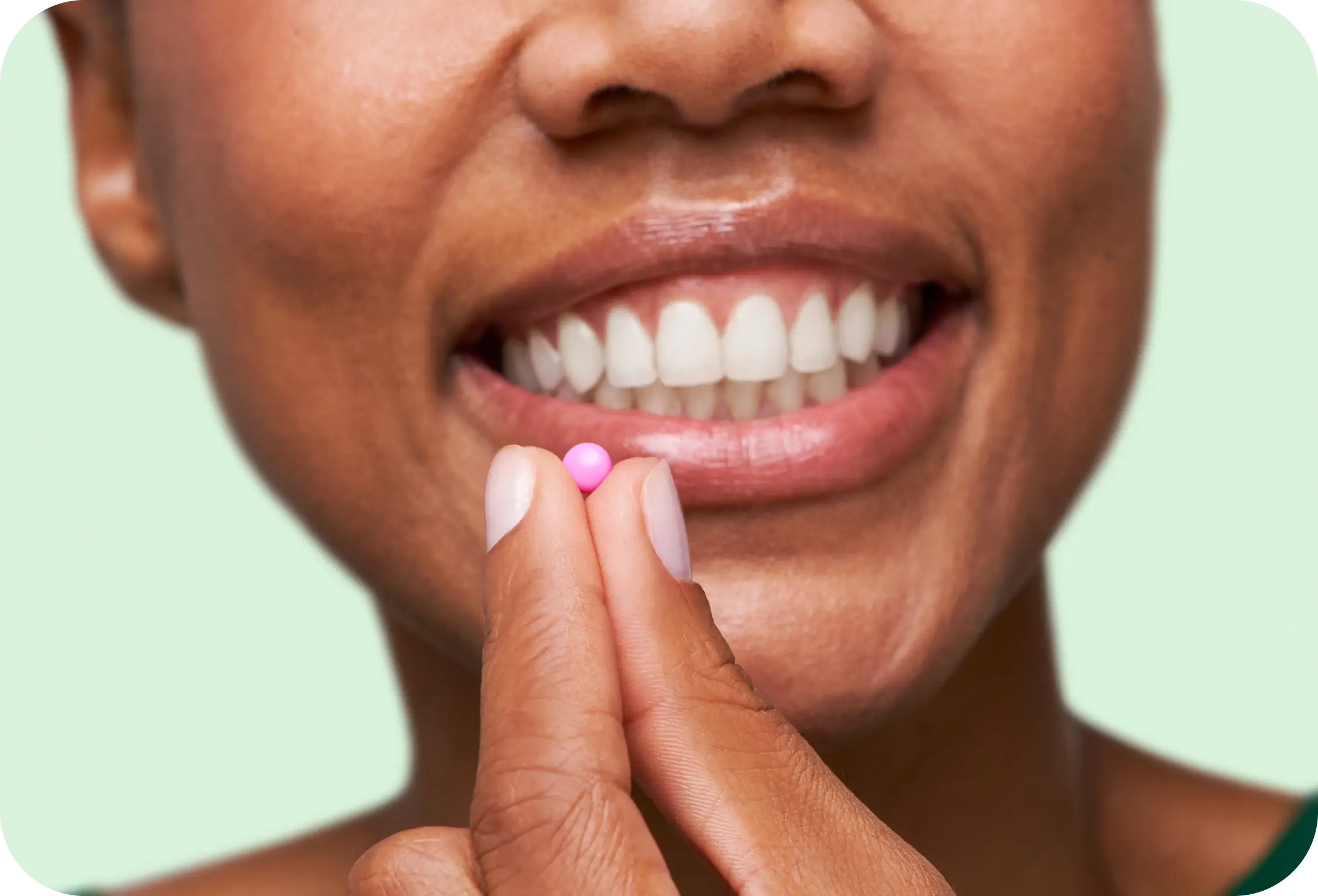 Person holding a small pink pill near their smiling mouth.