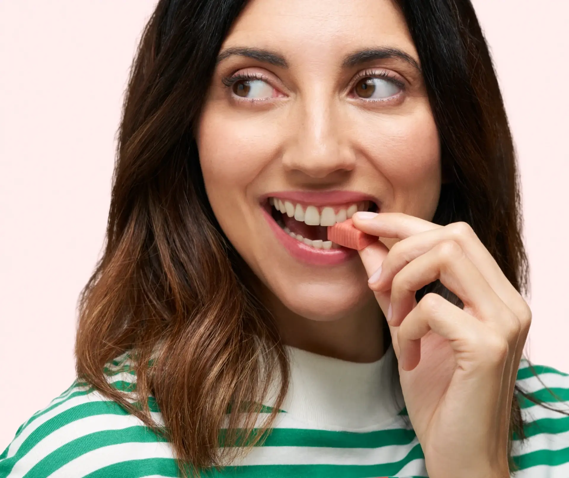 Close up shot of a smiling woman looking to the left about to take one piece of DulcoLax Soft Chews in front of a light pink background