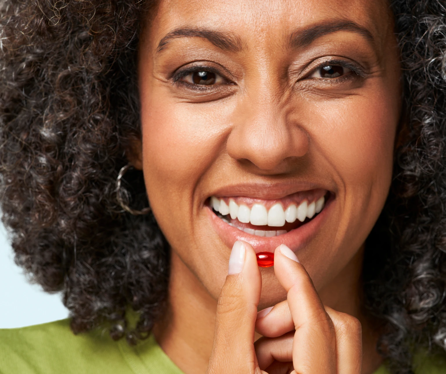 Smiling person holding a red capsule near their mouth.