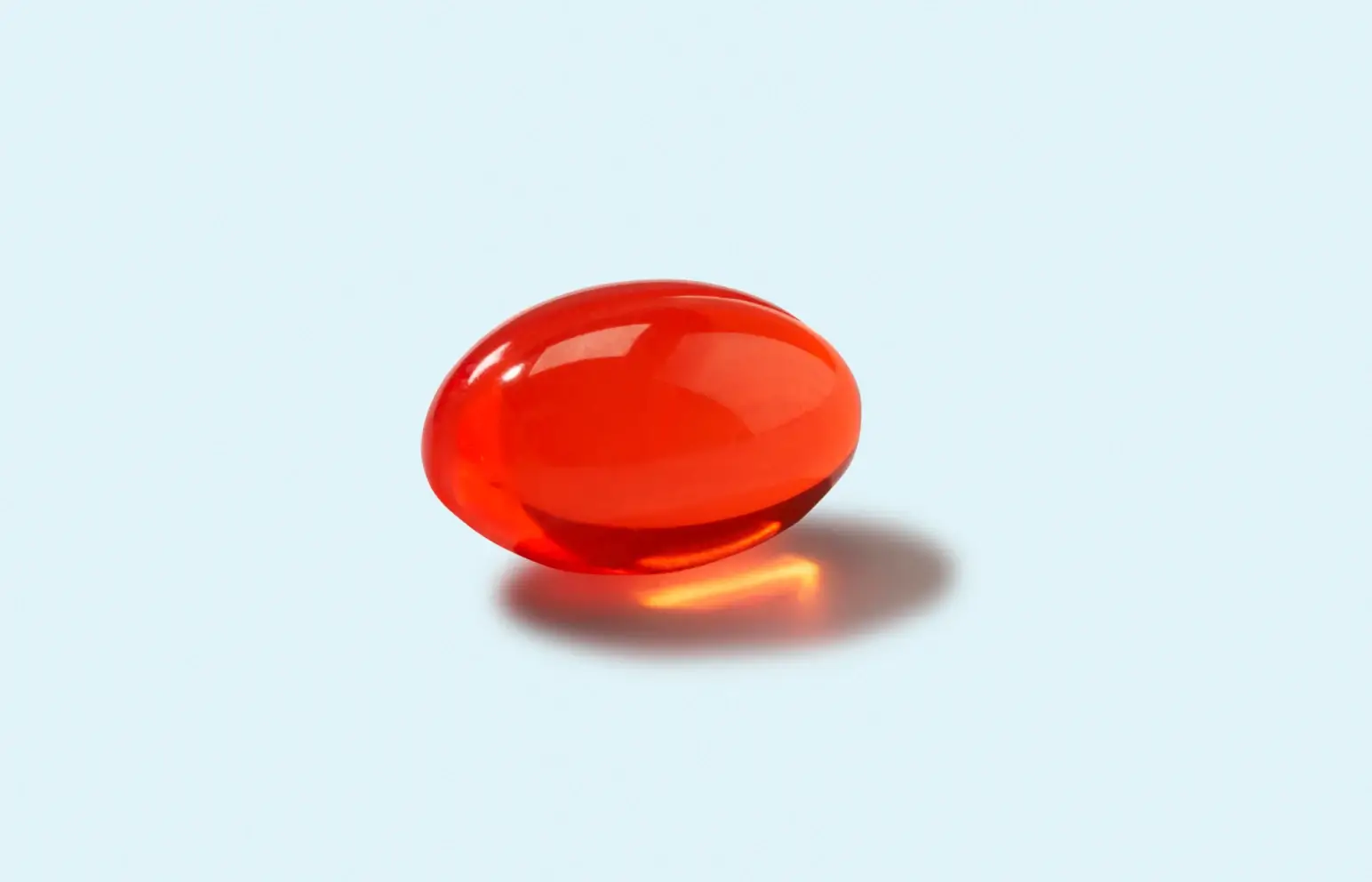 A single shiny red gel capsule on a light blue background.
