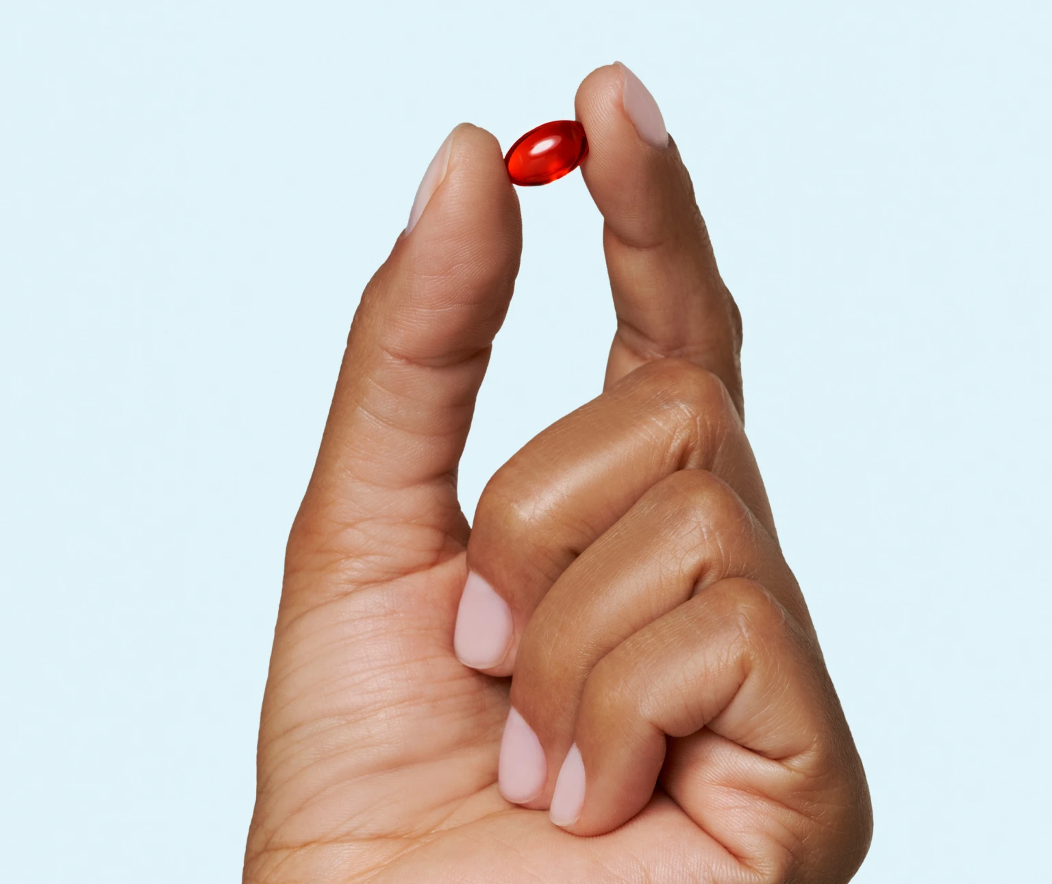 Hand holding a small red pill between fingers.