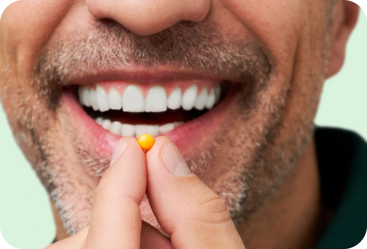 Man smiling while holding a small orange pill near his mouth.
