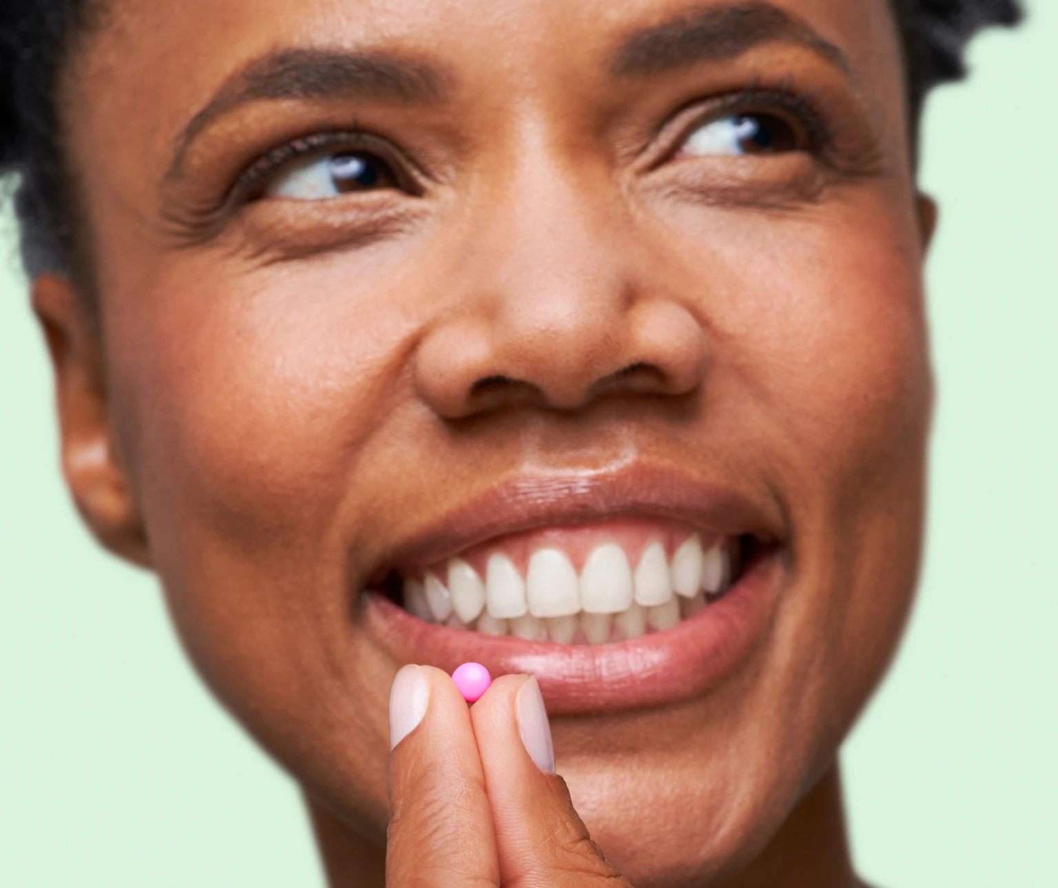 Close up shot of a smiling woman about to take one tablet of DulcoLax For Women in front of a light green background