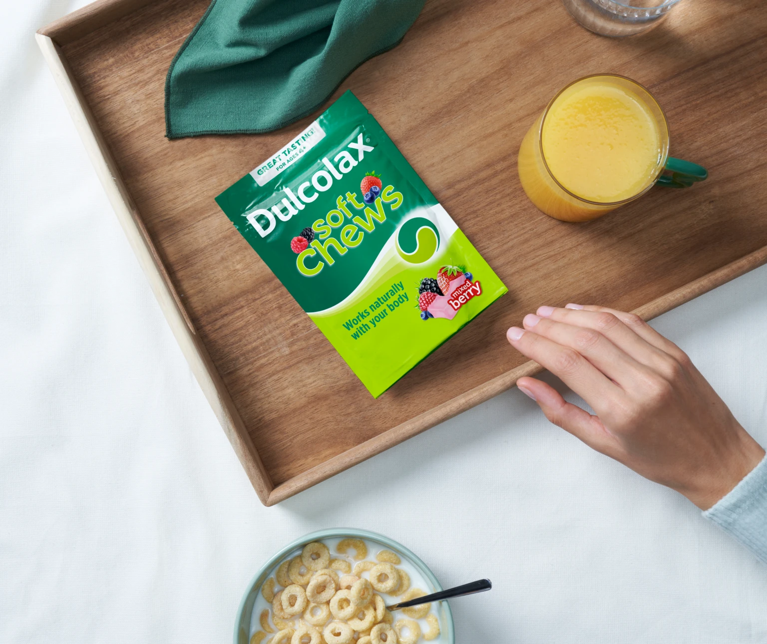 Dulcolax soft chews mixed berry on a tray with a hand, a bowl of cereal, and juice.