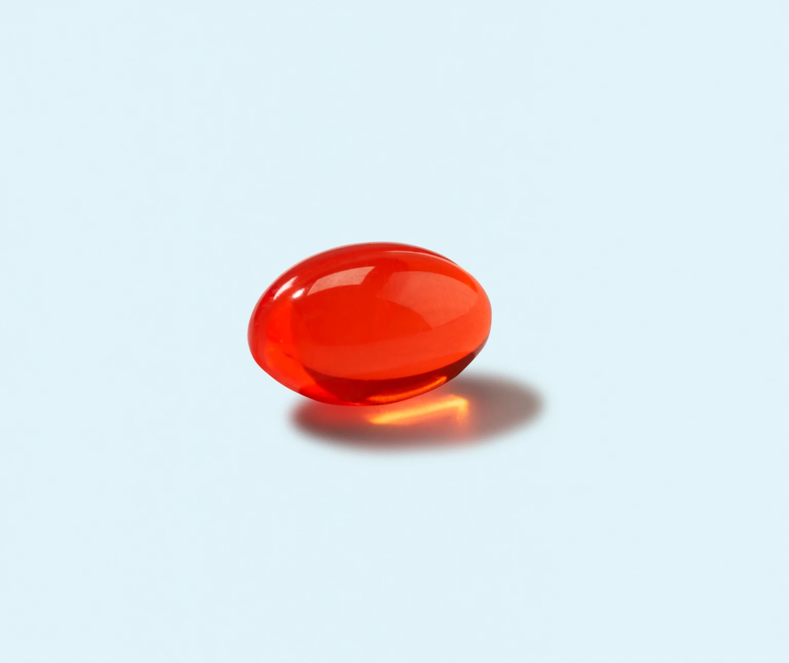 A single red softgel pill on a light blue background.